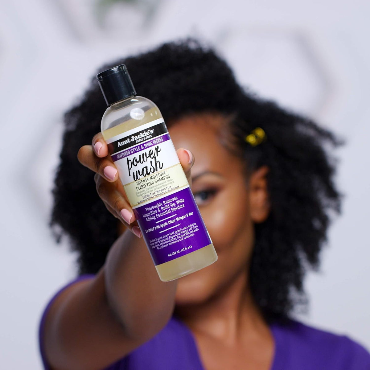 Kvinde der holder en flaske Aunt Jackie's Power Wash Intense Moisture Clarifying Shampoo.