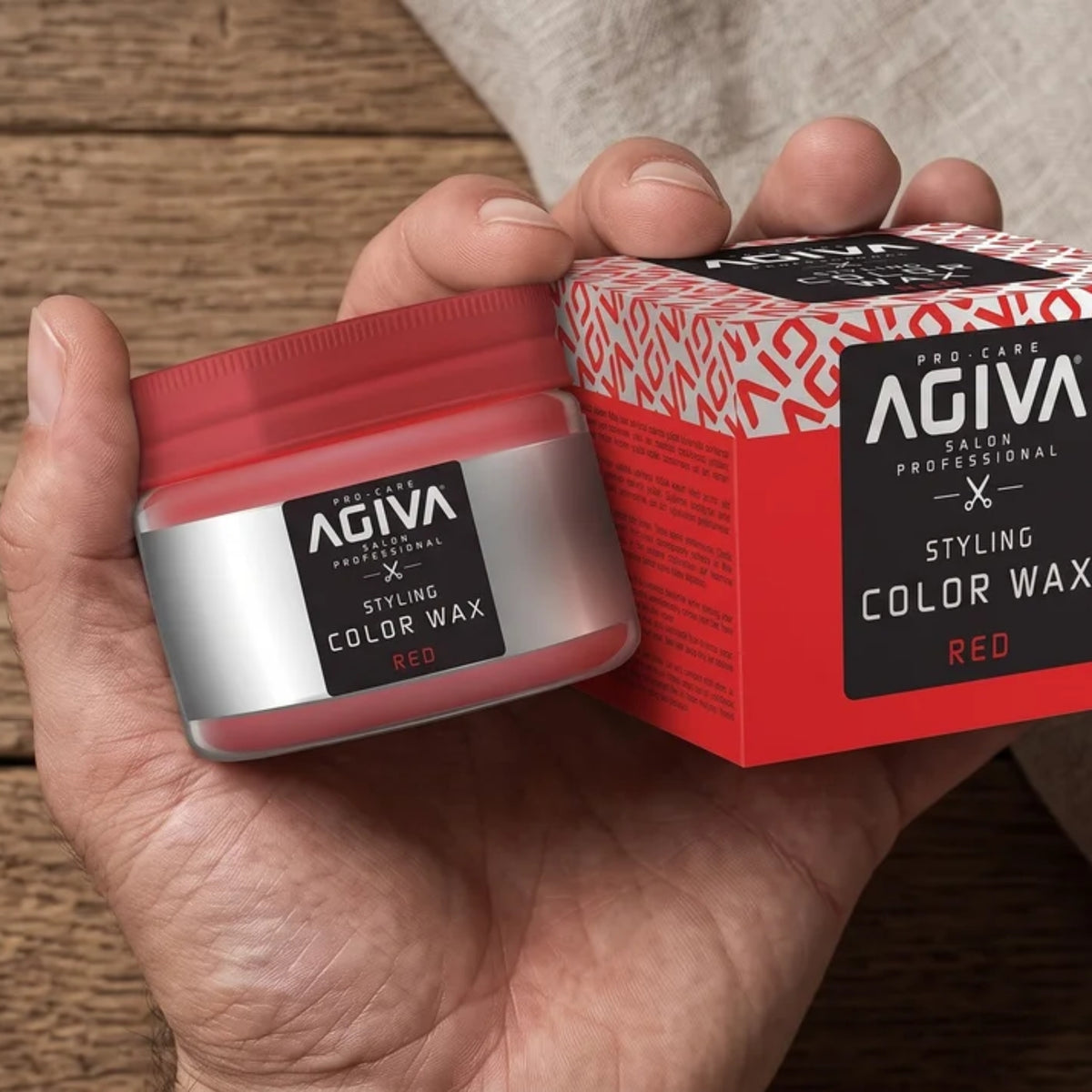 Hånd holder rød dåse med AGIVA Styling Color Wax i farven rød ved siden af den tilhørende røde emballageæske.