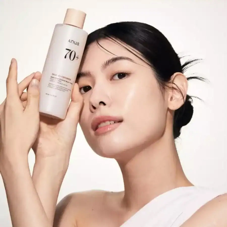 Kvinde med glødende hud holder Anua Rice 70 Glow Milky Toner 250ml op mod ansigtet foran lys baggrund.