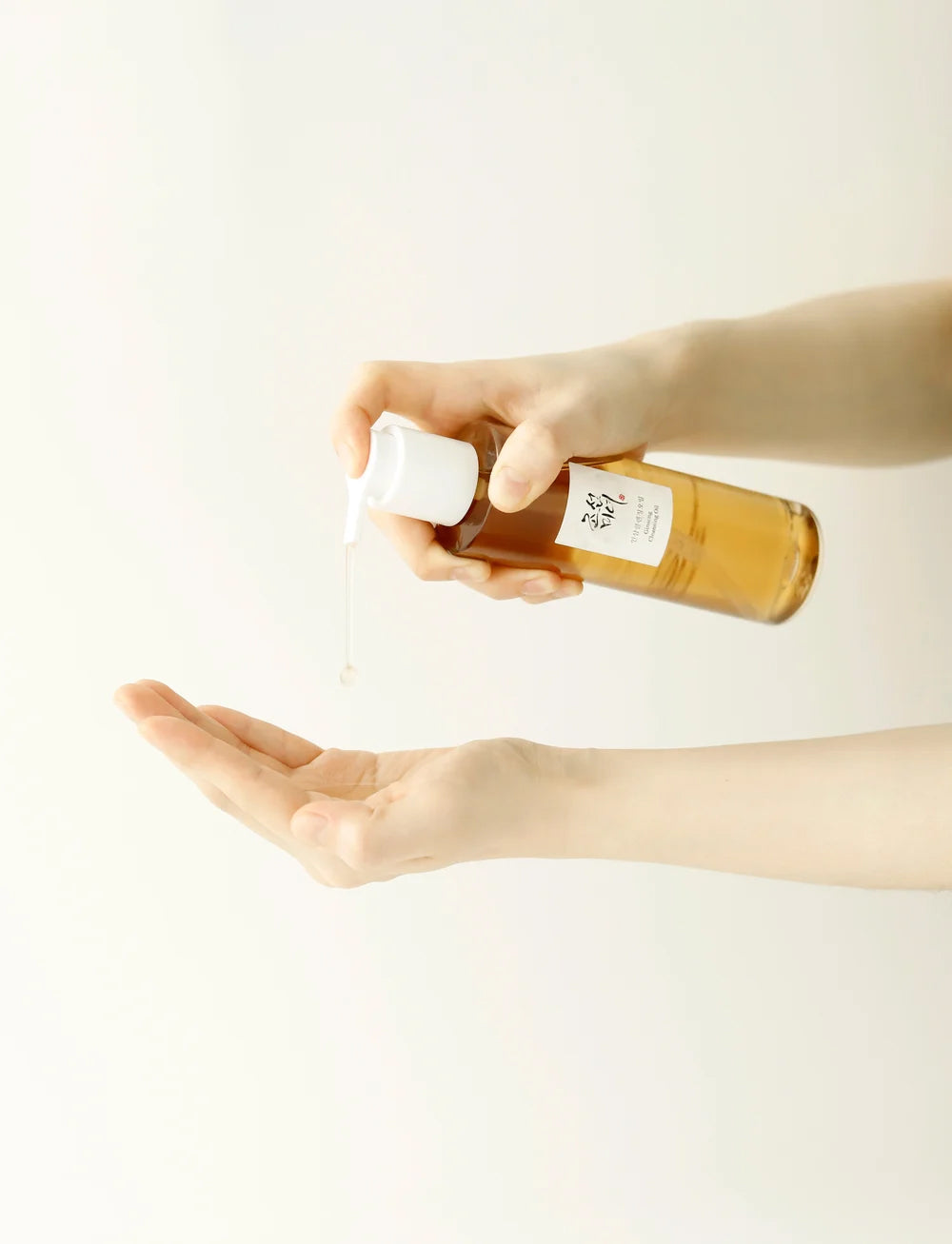 Beauty of Joseon Ginseng Cleansing Oil 210ml pumpes ud i håndfladen fra gylden flaske mod lys, minimalistisk baggrund.