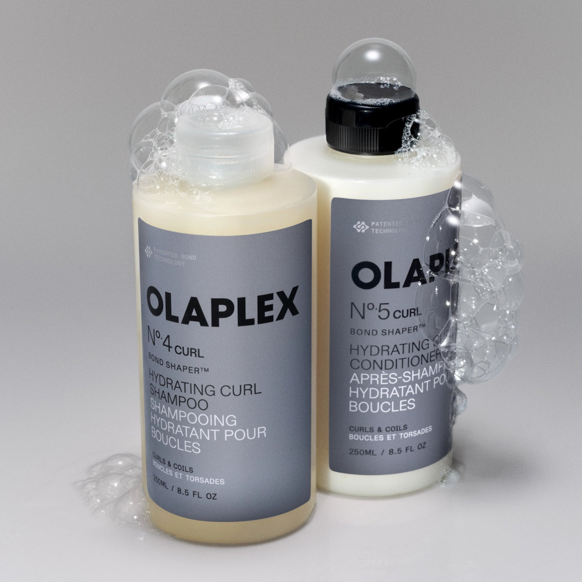 Olaplex No.4 Curl shampoo og No.5 Curl conditioner i 250 ml flasker omgivet af skum.