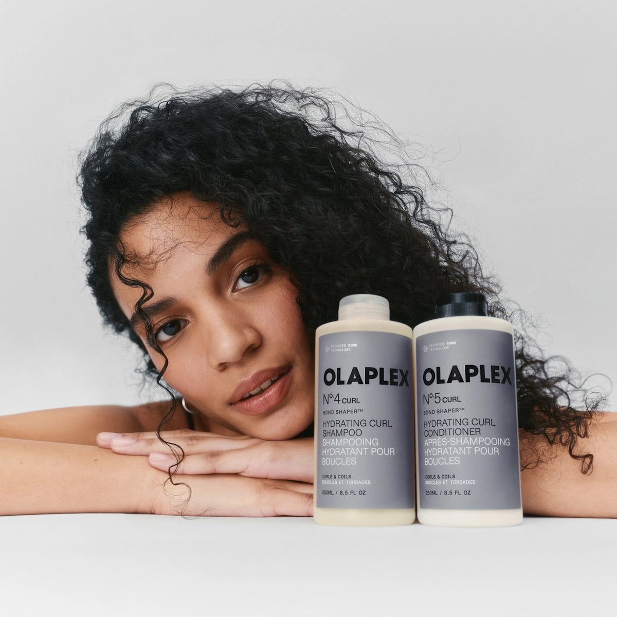 Kvinde med krøllet hår ved siden af Olaplex Nº.4 Curl shampoo og Nº.5 Curl conditioner til boucler.